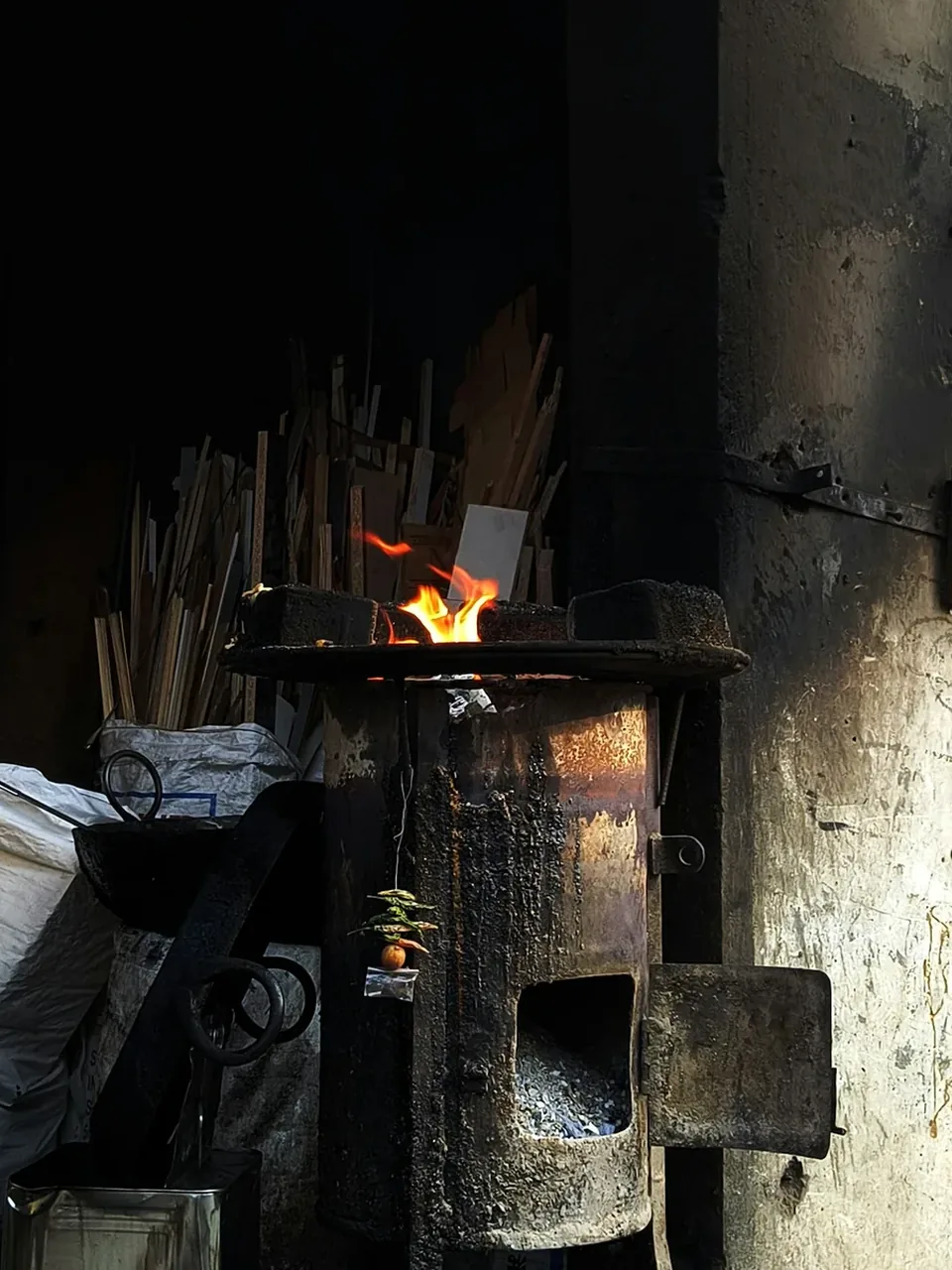 Horno de leña encendido en un taller de cerámica, con llama viva sobre la boca y herramientas apoyadas al lado